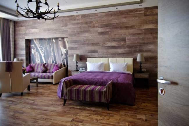 Двуспальная кровать в комнате в натуральном стиле с люстрой, стилизованной под оленьи рога.