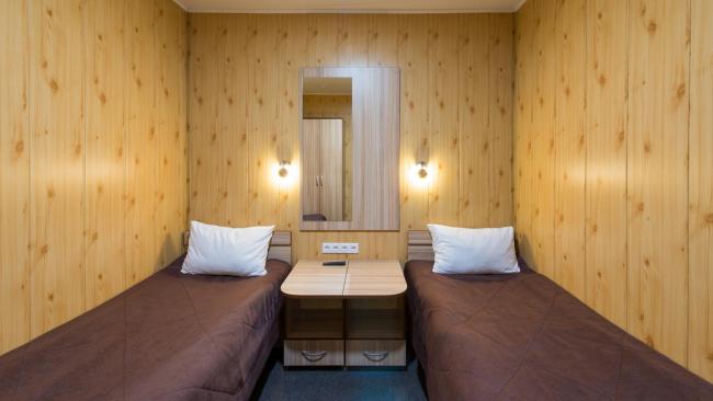 Маленький номер с двумя кроватями, прикроватной тумбочкой и светильниками на стене.
