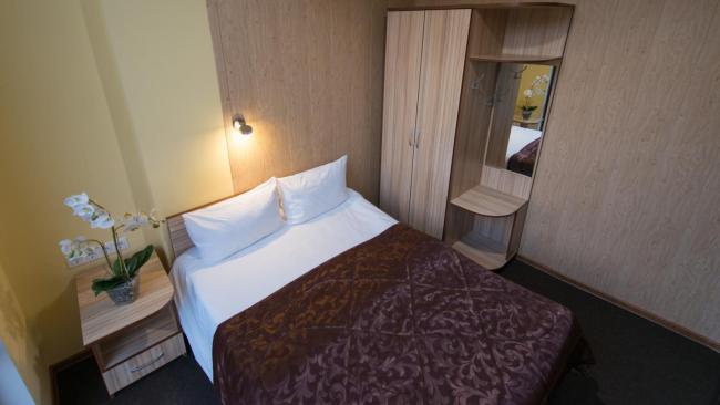 Двуспальная кровать в комнате со шкафом для одежды, прикроватной тумбой и французским окном.