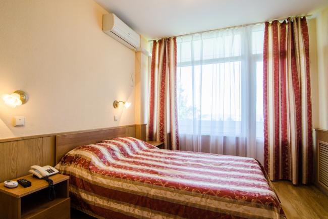 Двуспальная кровать с прикроватными тумбочками и светильником в номере.